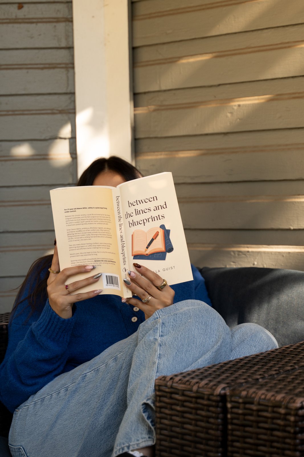 Gabriella reading Between the Lines and Blueprints on a cozy porch chair