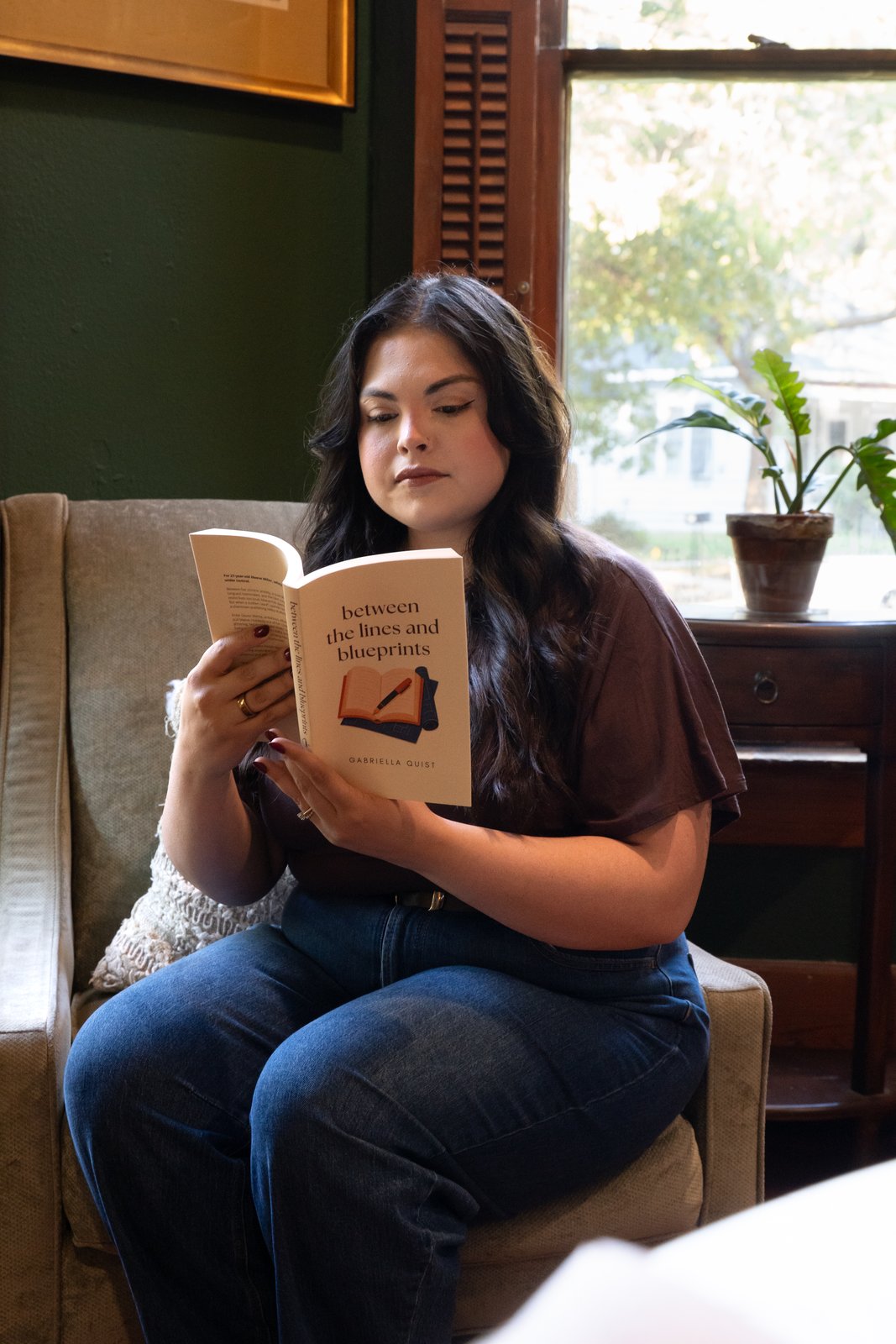 Gabriella reading Between the Lines and Blueprints in an armchair